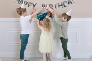Joyful children celebrate a birthday, exchanging gifts indoors.