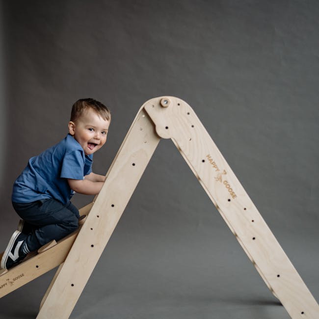 A cheerful young boy in blue shirt climbing a wooden ladder indoors. Nachhaltige Geschenke mit Holzspielzeug