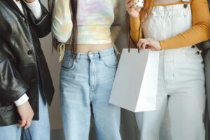 Three young women in casual attire with a gift bag, enjoying a relaxed indoor setting.