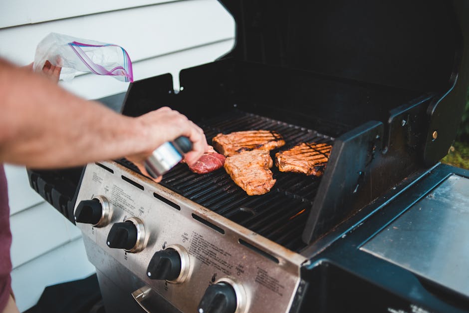 A man seasons steak on a grill for a backyard barbecue, displaying outdoor cooking.