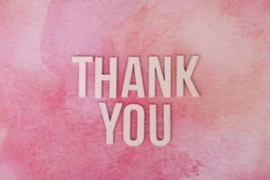 Express gratitude creatively with this 'Thank You' design featuring wooden letters on a pink background.