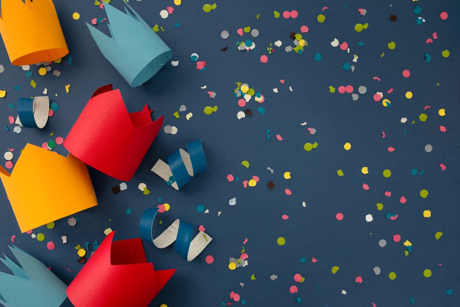 Vibrant paper crowns and multicolored confetti create a festive, creative scene.
