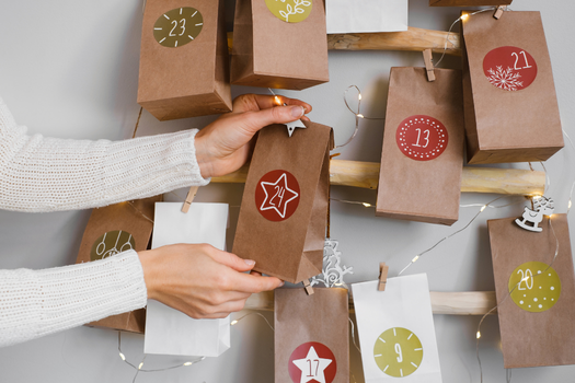 Kraftpapiertüten mit Zahlen für den Adventskalender. Eine Frau nimmt eine Tüte ab, die an der Wand hängen.