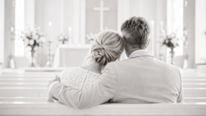ein Paar in festlicher Kleidung in einer Kirche sitzend auf der Bank bei ihrer Silberhochzeit