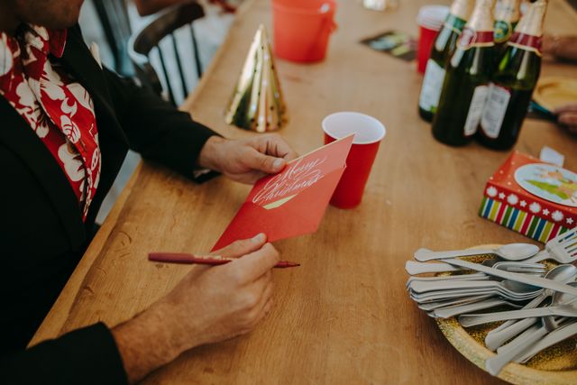 Man writing a Christmas card at a festive holiday party with drinks and decorations.